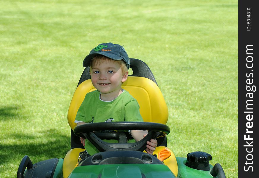 A young boy sitting on a riding mower under a shade tree outside in a large Field. A young boy sitting on a riding mower under a shade tree outside in a large Field