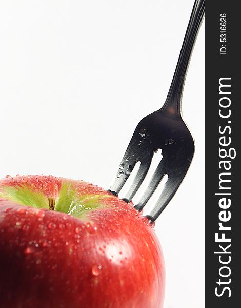 A fork sticks out of a red juicy apple against a white background. A fork sticks out of a red juicy apple against a white background.