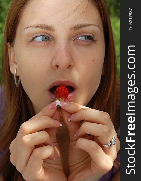 Beautiful young woman with nice long hair is eating a small strawberry. Beautiful young woman with nice long hair is eating a small strawberry.