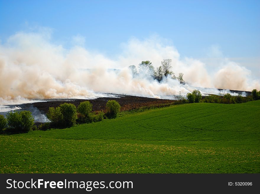 Farmland on fire with clouds of smoke and green pasture. Farmland on fire with clouds of smoke and green pasture