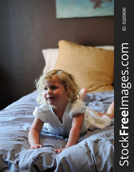 A happy little girl with blonde hair and a white dress plays on her parents bed. A happy little girl with blonde hair and a white dress plays on her parents bed.