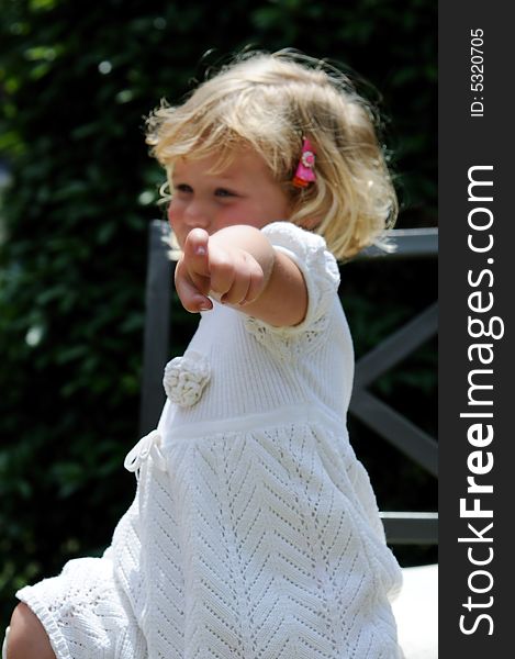 Little girl points at the viewer while sitting in a garden chair. Little girl points at the viewer while sitting in a garden chair.