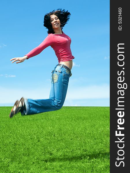 Woman jump in green field under blue sky