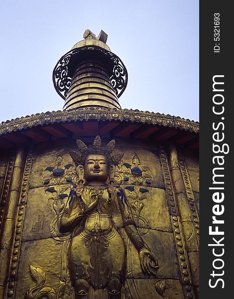 Close-up of a buddha sculpture on a huge copper prayer wheel