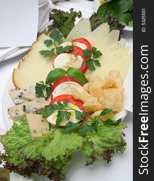 Plate with different kinds of cheese and a tomato.