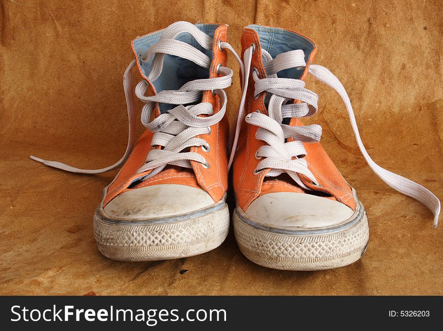 Pair of used orange sneakers on brown background