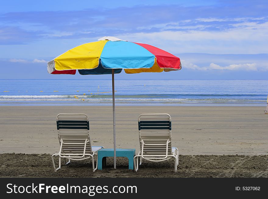 Two beach chairs under a colorful umbrella