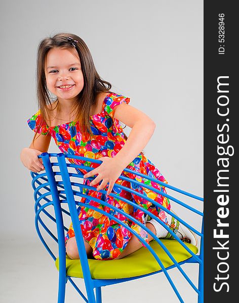 Little cute laughing brown-haired girl in red dress sitting on a chair. Little cute laughing brown-haired girl in red dress sitting on a chair