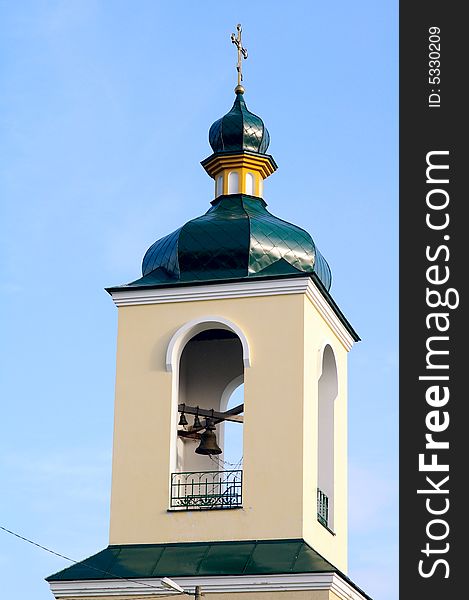 Fragment of church with the bell against the background of the blue sky. Fragment of church with the bell against the background of the blue sky