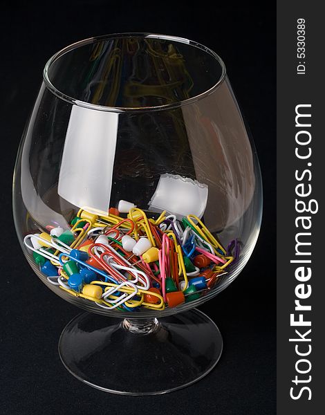 Colored paperclips and pins in a glass on a black background. Close up. Selective focus.