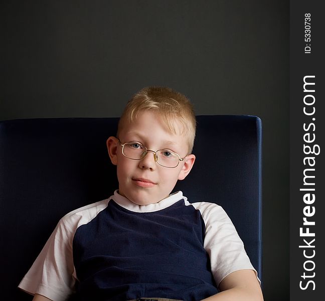 Confident boy sit on chair and look at camera. Over grey background.