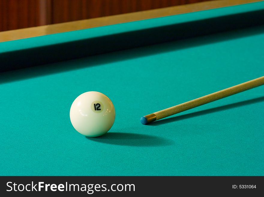 The white billiard-ball number 12 and wood cue on a green table. The white billiard-ball number 12 and wood cue on a green table