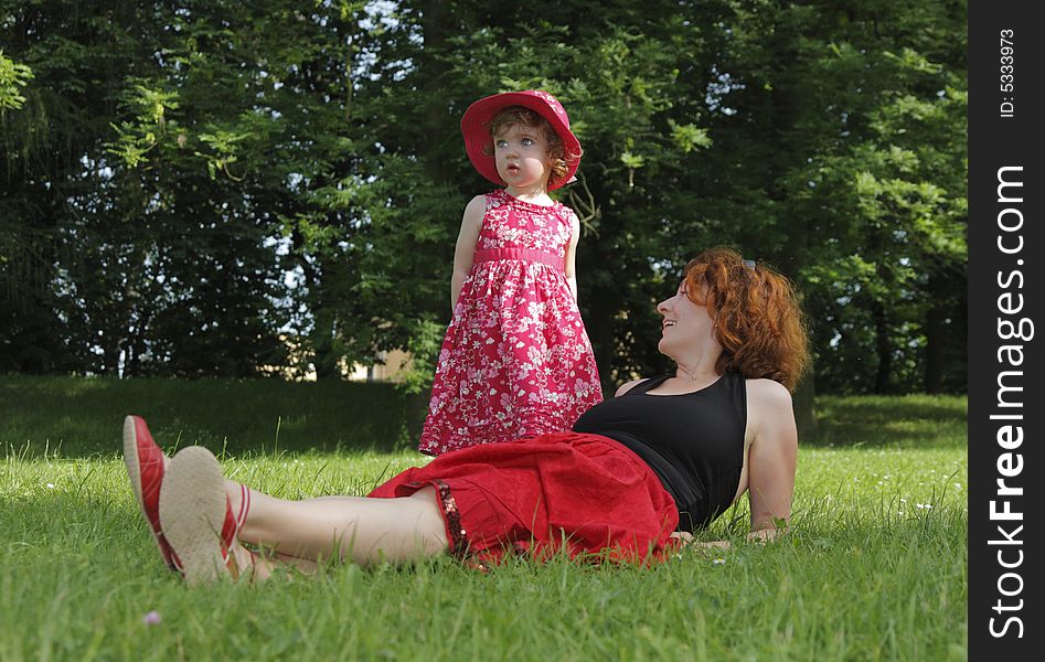 A happy woman is lying on the grass. Her daughter is standing near.