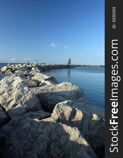 Trail of large boulders and lighthouse. Beautiful lake and clear sky. Trail of large boulders and lighthouse. Beautiful lake and clear sky.