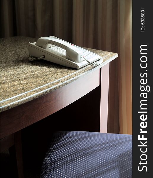 A white business phone on a desk, with a chair and lateral light.