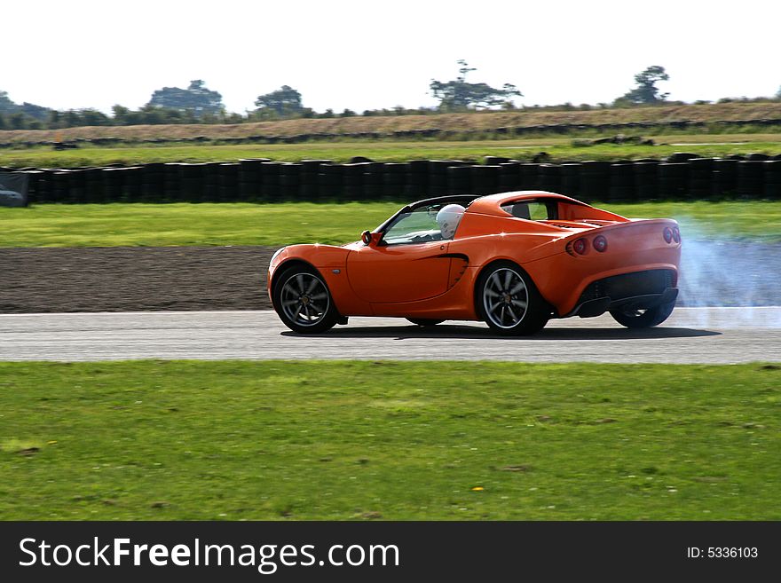 Orange sportscar on the track with smokey tires