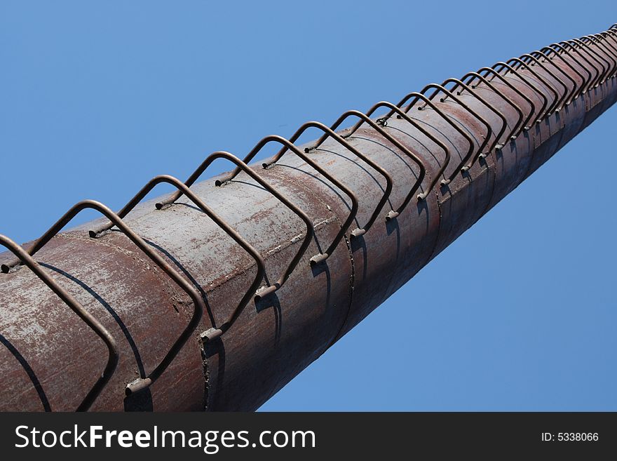 The rusty pipe with leaves in a distance on a background of the blue sky. The rusty pipe with leaves in a distance on a background of the blue sky