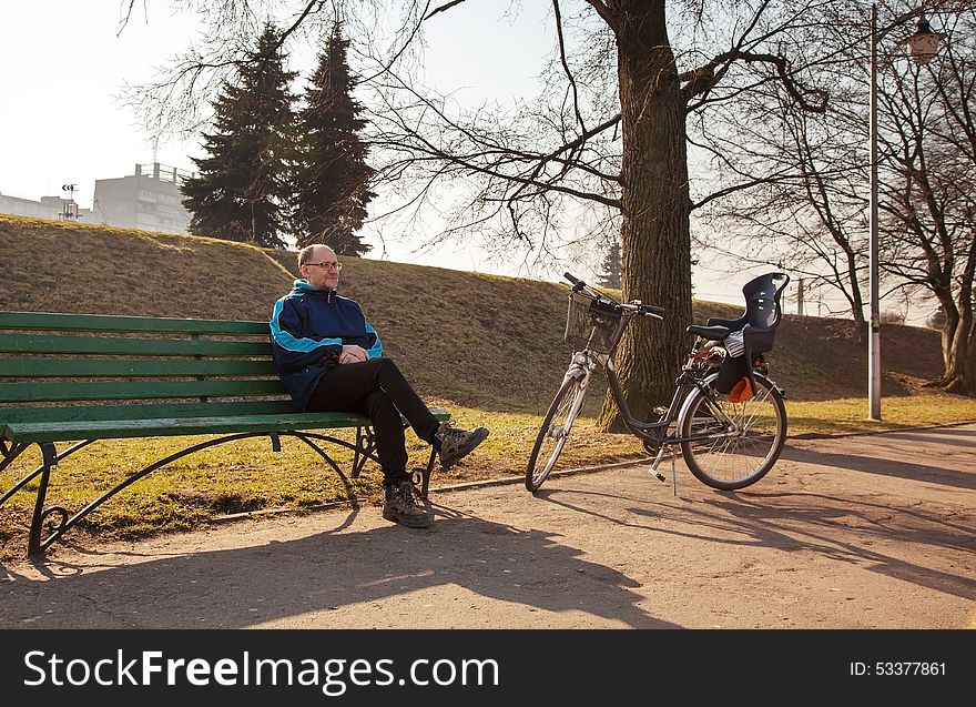 Elderly man sitting on a bench near his bicycle in a city park