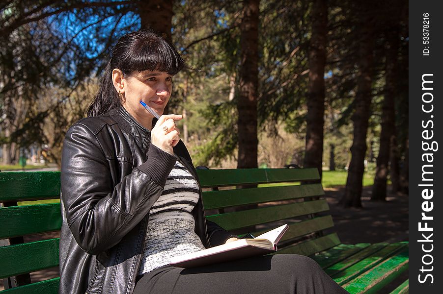 Beautiful Woman Sitting On A Park Bench Holding A Pen And Notebo