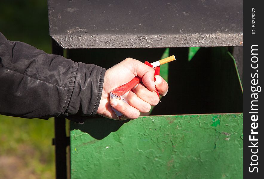 Man&#x27;s hand breaks a pack of cigarettes about a waste bin closeup outside