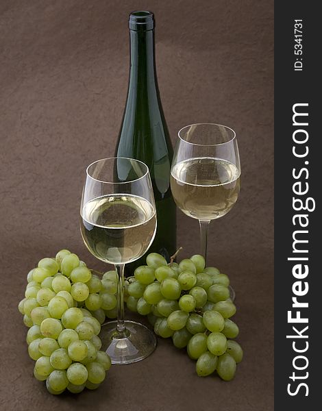 White wine with bottle, glasses and grapes against a background