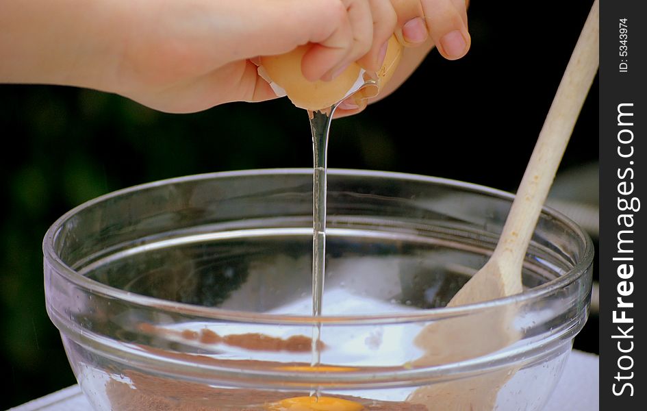 Shot of a child cracking an egg into cake mixture