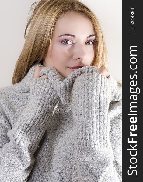 Beautiful blond girl in grey jersey hiding behind the neck and looking at the camera