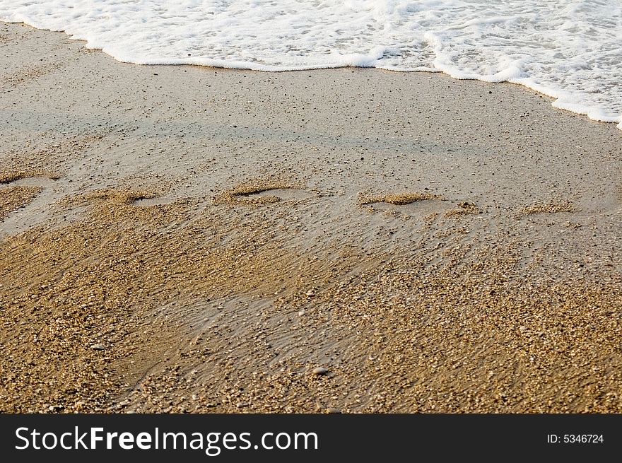 Waves crashing up to the sand beach, on beach footprint