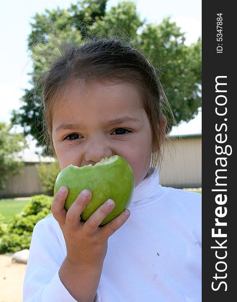 A young school age girl eats a green apple for a healthy snack. A young school age girl eats a green apple for a healthy snack