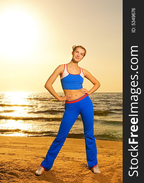 Beautiful young woman doing fitness exercise on a beach at sunset