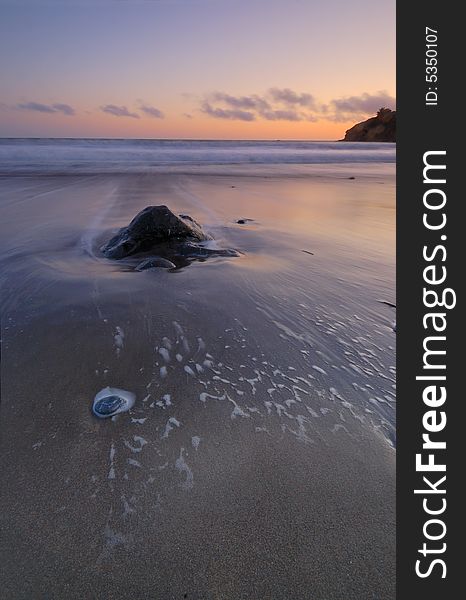 A rock on the shoreline at sunset