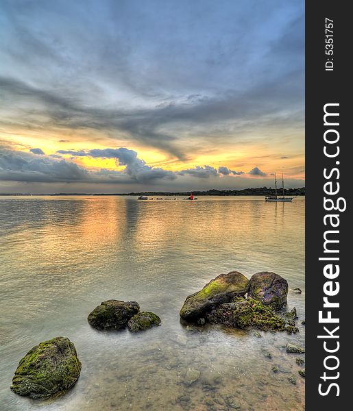 A cluster of rocks on a beach opposite a beacon and a moored yacht as seen at an overcast sunset. A cluster of rocks on a beach opposite a beacon and a moored yacht as seen at an overcast sunset