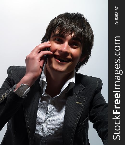 A portrait about a trendy attractive young man who is smiling and he is ringing up somebody. He is wearing a white shirt and a stylish black suit. A portrait about a trendy attractive young man who is smiling and he is ringing up somebody. He is wearing a white shirt and a stylish black suit.