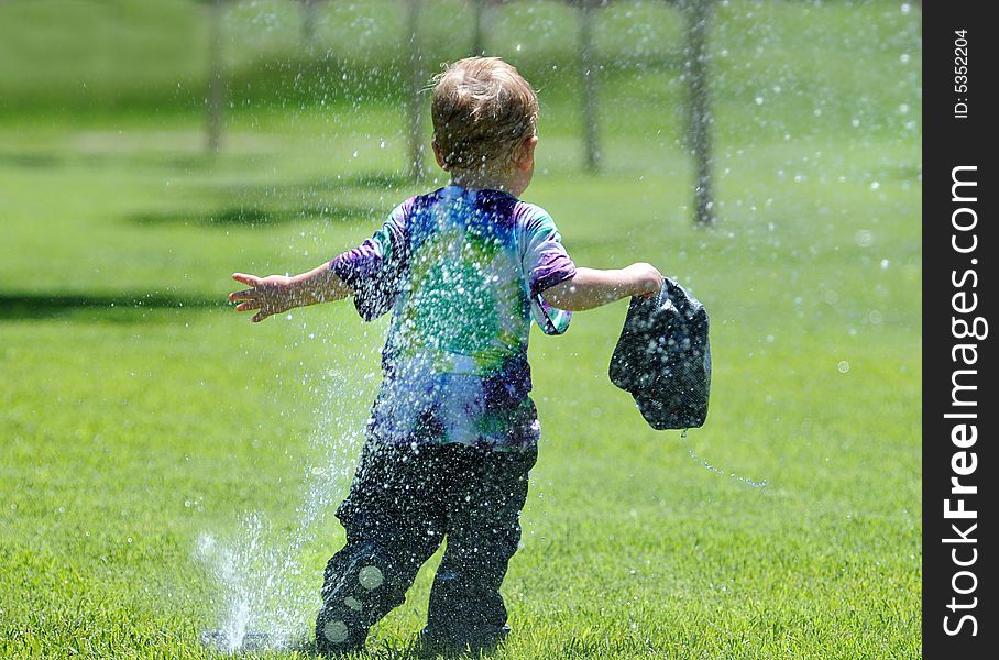 Young boy running away from water sprinkler trying not to get wet. Young boy running away from water sprinkler trying not to get wet