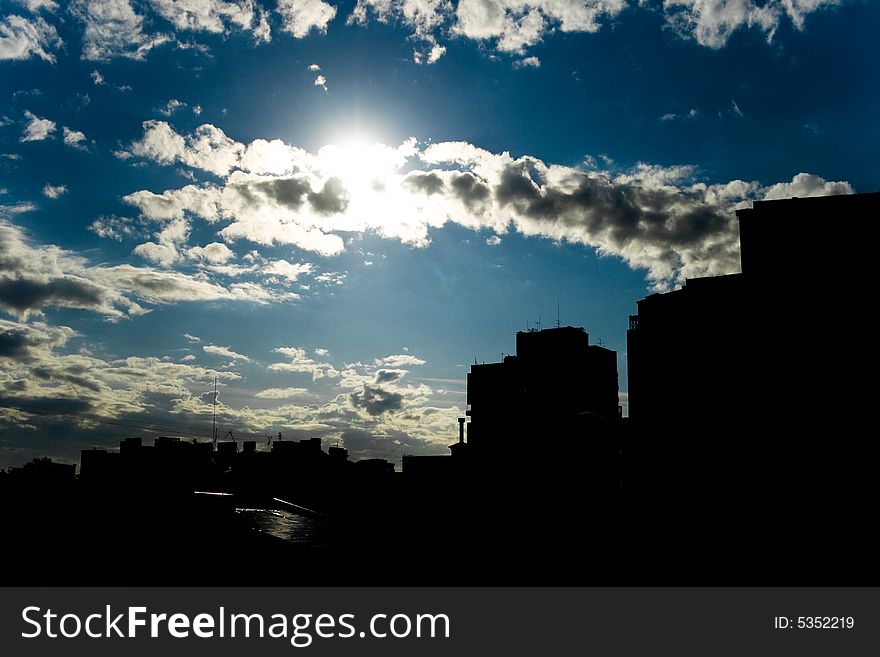 Sunny day, the sun covered by clouds, silhouettes of buildings. Sunny day, the sun covered by clouds, silhouettes of buildings