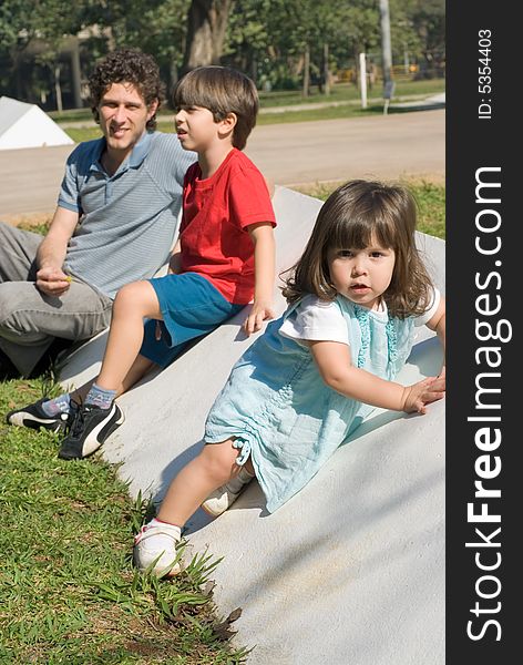 Vertically framed outdoor shot of a father, his son, and his daugther sitting in a park on a sunny day. Vertically framed outdoor shot of a father, his son, and his daugther sitting in a park on a sunny day.