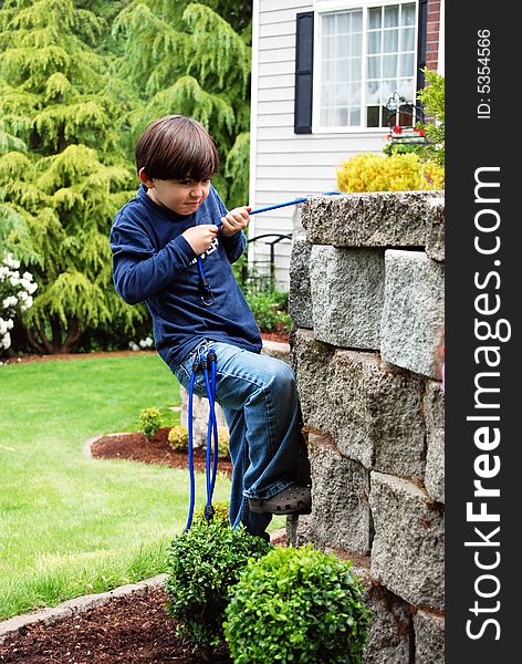 Adorable little boy top roping and climbing a stone garden wall using bungee cords as climbing rope. Vertically framed shot in which he looks focused his goal. Adorable little boy top roping and climbing a stone garden wall using bungee cords as climbing rope. Vertically framed shot in which he looks focused his goal.