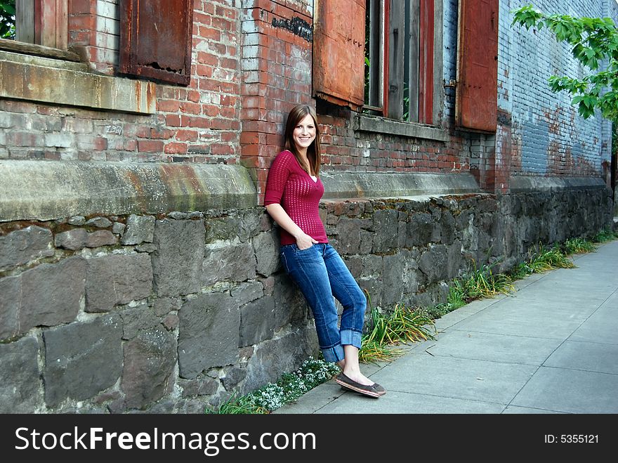 Horizontally framed outdoor shot of a smiling teenage girl with her hands in her pockets leaning against a brick and stone wall. Horizontally framed outdoor shot of a smiling teenage girl with her hands in her pockets leaning against a brick and stone wall.