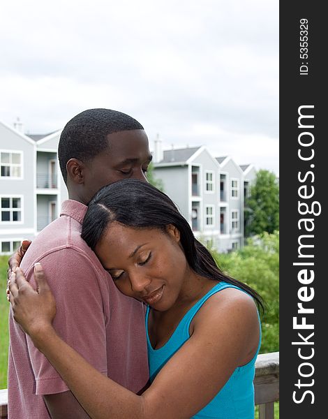 Attractive young couple in a embrace, with the womans head resting on the mans shoulder. Vertically framed outdoor shot on a deck. Attractive young couple in a embrace, with the womans head resting on the mans shoulder. Vertically framed outdoor shot on a deck.