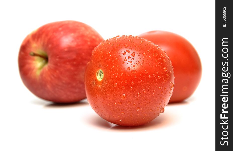 Red apple and tomatoes covered by drops of water on the white background. Isolated. Shallow DOF.