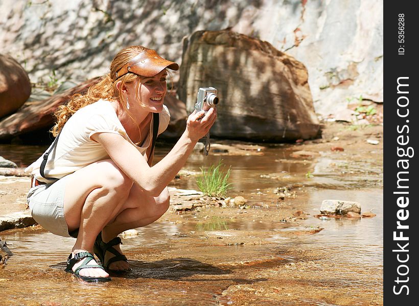A beautiful young redhaired woman in a leather visor enjoys using her digital camera on a sunny day at the creek. A beautiful young redhaired woman in a leather visor enjoys using her digital camera on a sunny day at the creek.