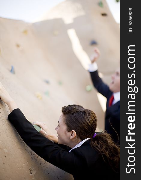 Businesswoman climbs as businessman loses grip and falls away from wall. Businesswoman climbs as businessman loses grip and falls away from wall