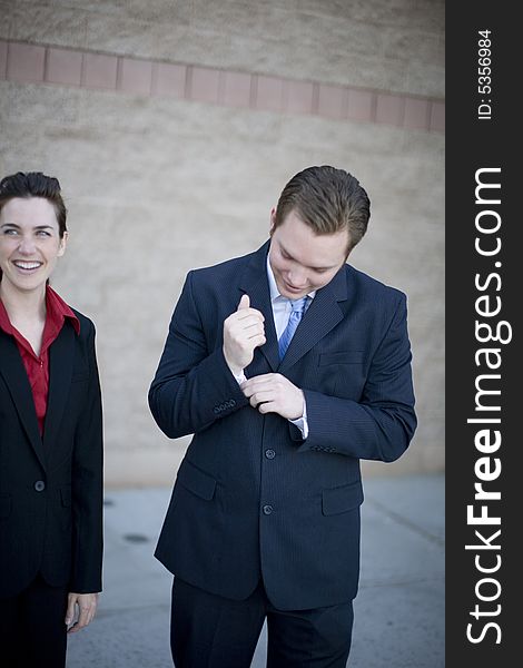 Businessman and businesswoman stand together smiling while man fixes shirt. Businessman and businesswoman stand together smiling while man fixes shirt