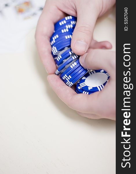 Man is holding a set of blue gambling chips in his hands waiting to make his bet with cards blurred in the background. Man is holding a set of blue gambling chips in his hands waiting to make his bet with cards blurred in the background