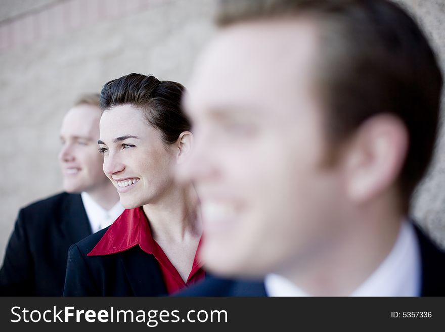 Three businesspeople standing in a line with young attractive woman in the middle smiling. Three businesspeople standing in a line with young attractive woman in the middle smiling