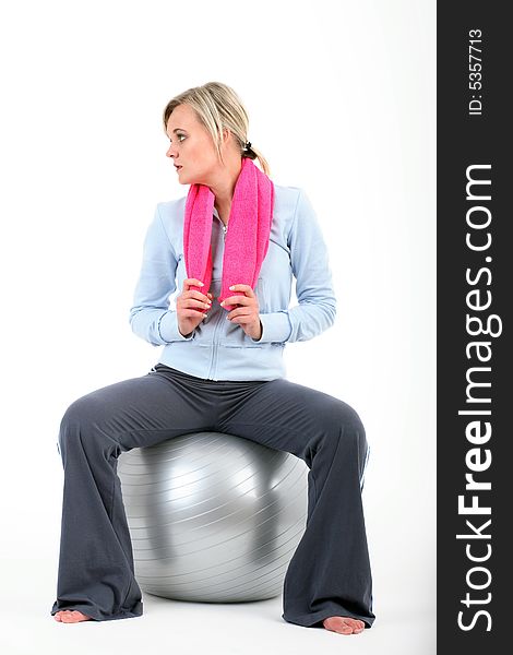 Blond woman in gym outfit exercising with a pilates ball holding a pink towel isolated on white