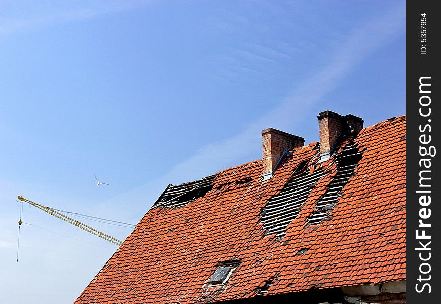 Deavastated roof closeup with yellow crane and bird in background. Huge holes in the red roof after fire.