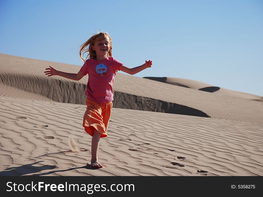 Horizontal shot of a young, six year old, girl wandering on a desolate sand dune in the deep desert. Horizontal shot of a young, six year old, girl wandering on a desolate sand dune in the deep desert