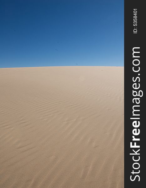 An image of rolling sand dunes with a blue sky