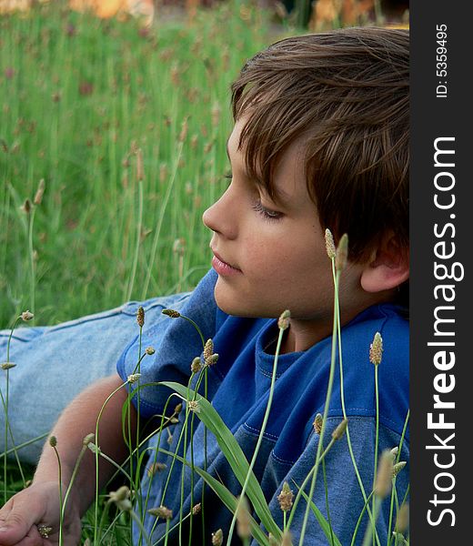 Boy in blue t-shirt lying in the grass not looking at the camera. Boy in blue t-shirt lying in the grass not looking at the camera